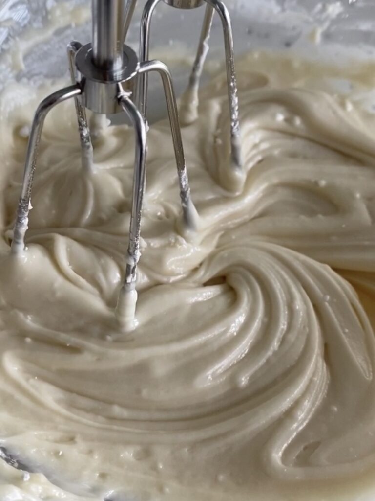 mixing vegan cream cheese frosting using a hand mixer. 
