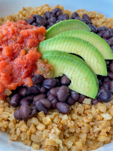 Cauliflower burrito bowl topped with black beans, salsa and avocado slices.