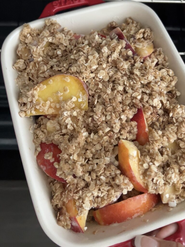Peaches in a white baking dish with oatmeal mixture on top. 