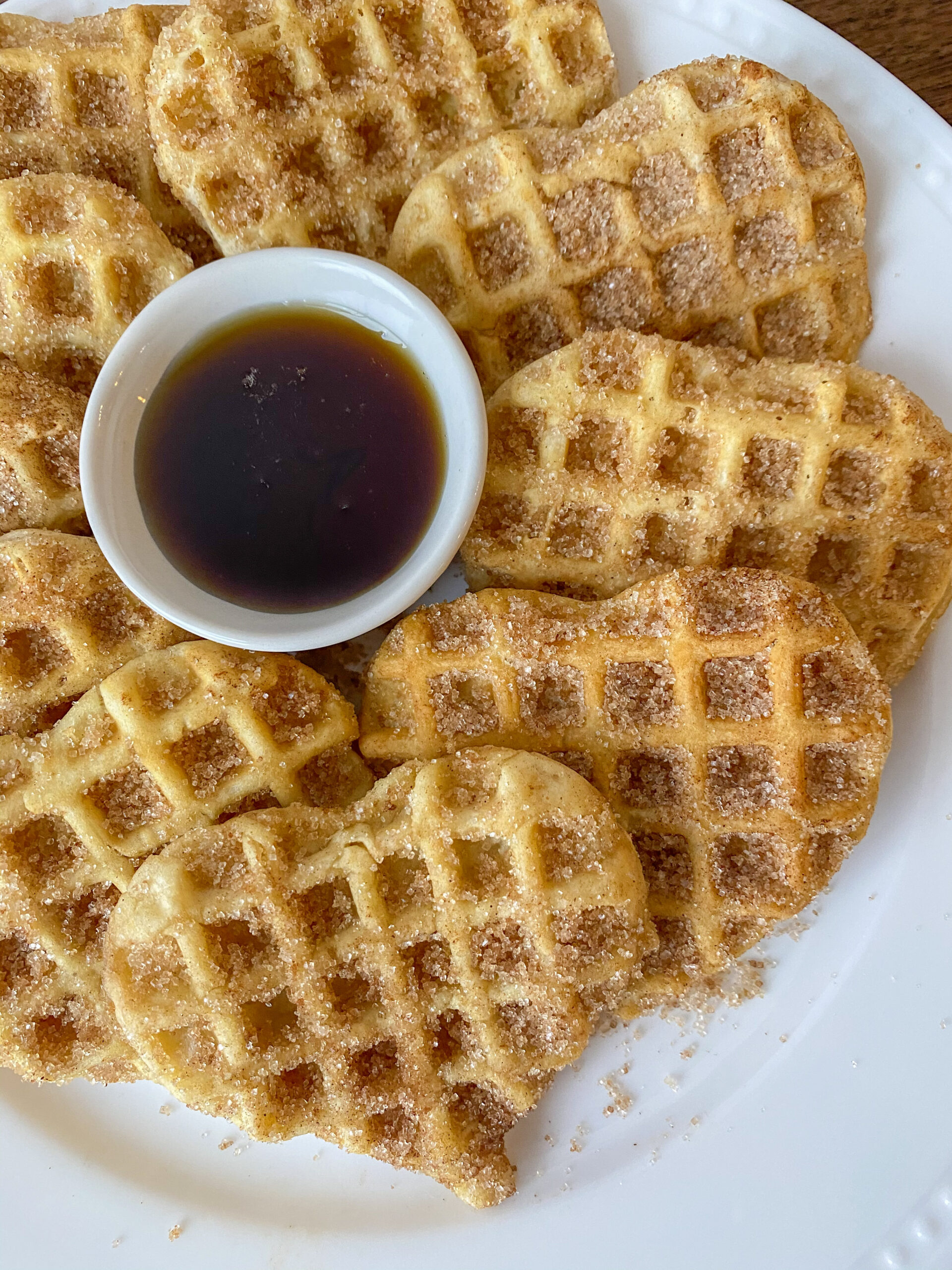 cinnamon sugar waffles in a circle on a white plate with a cup of maple syrup in the middle. 