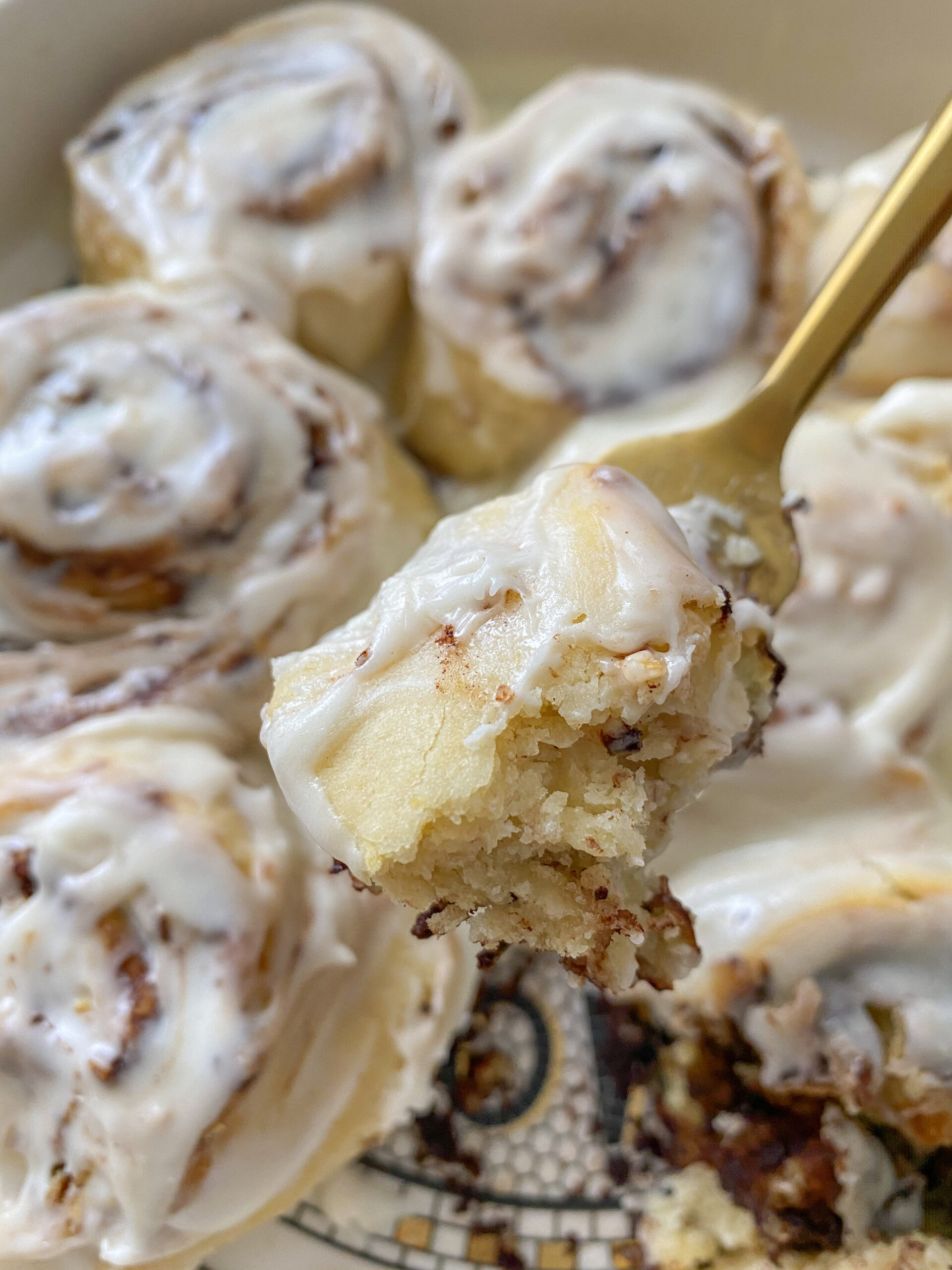 Bite of cinnamon roll on a fork with no yeast cinnamon rolls in the background. 