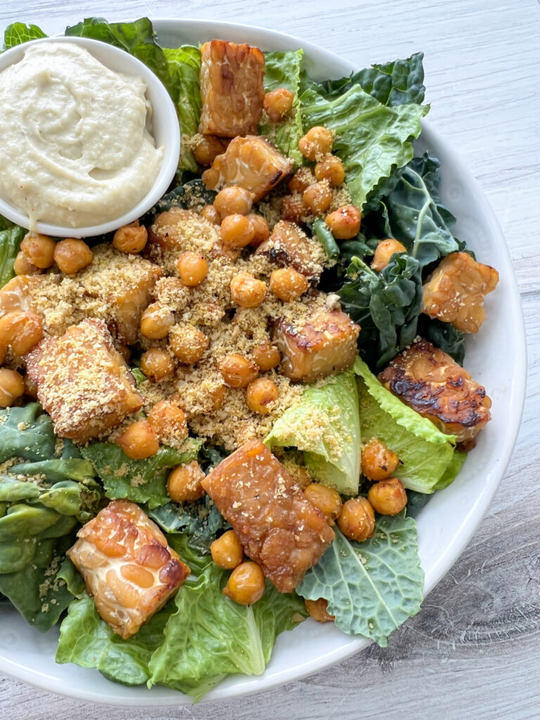 Vegan caesar salad with chickpeas and tempeh and dressing on the side. 