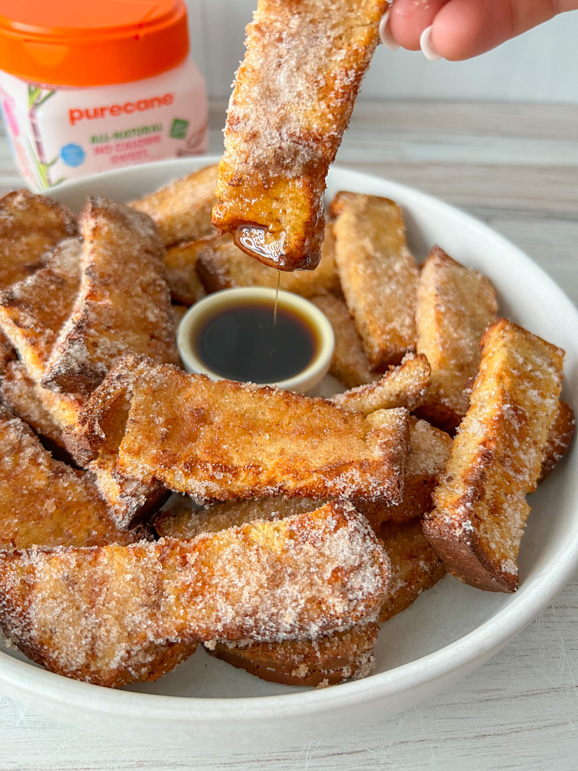 Dipping air fryer french toast sticks into maple syrup.