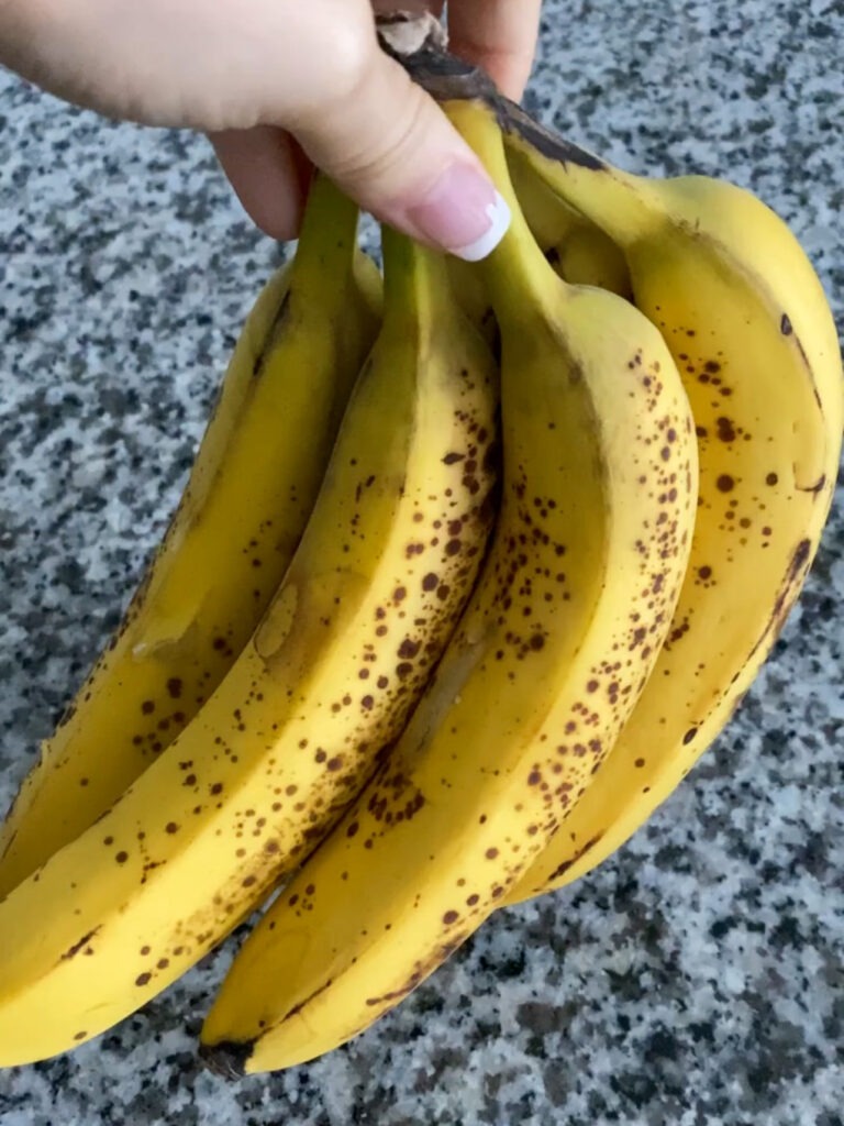 Spotted bananas being held by a woman's hand.