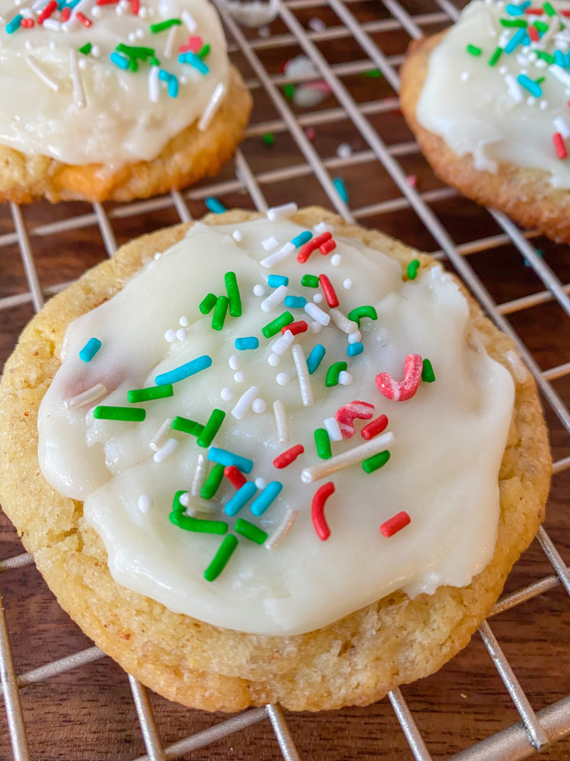 sugar cookie with white icing and sprinkles on top, sitting on a cooling rack. 