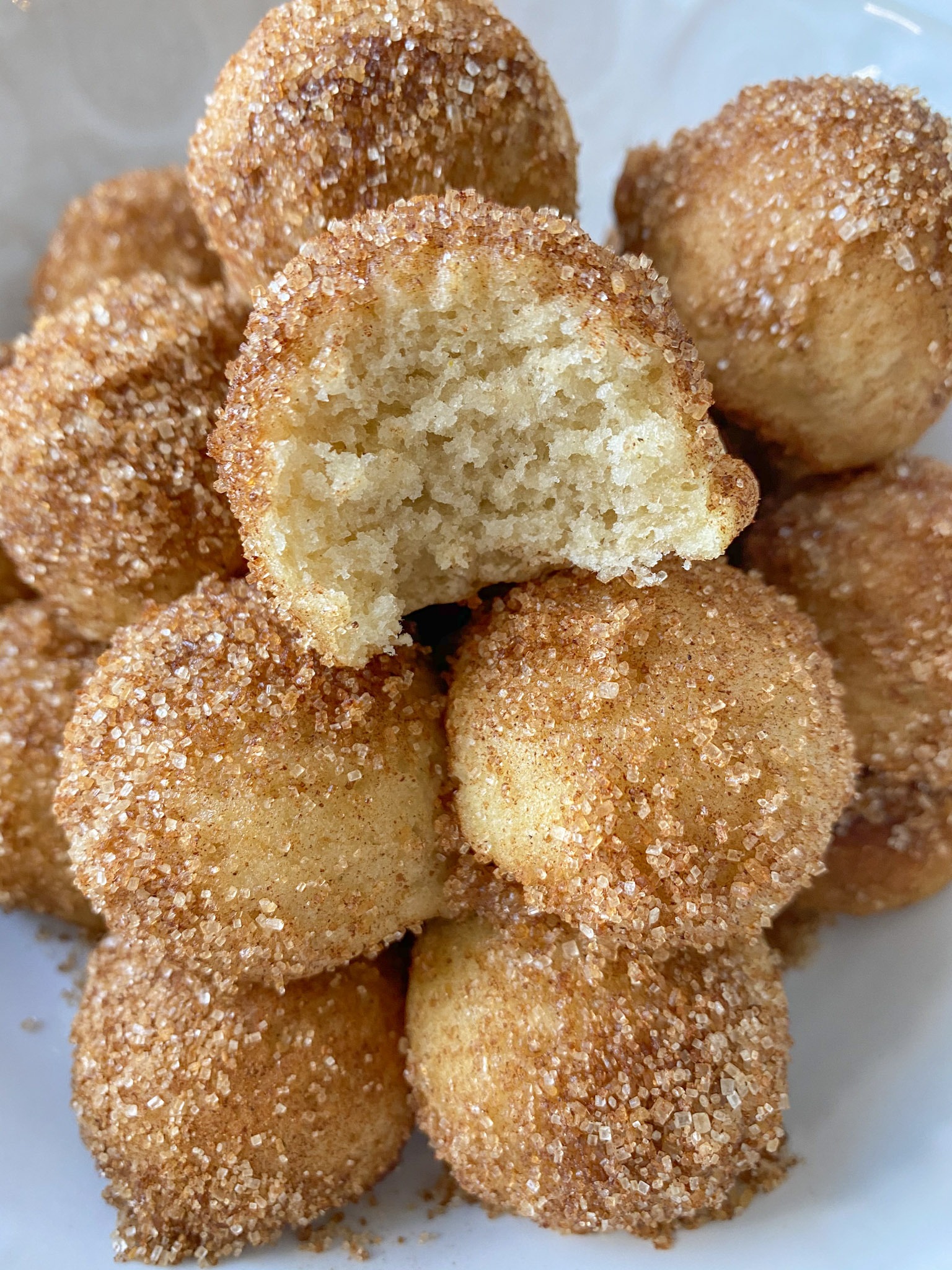 cinnamon sugar donut holes stacked on a plate with the top donut hole missing a bite.