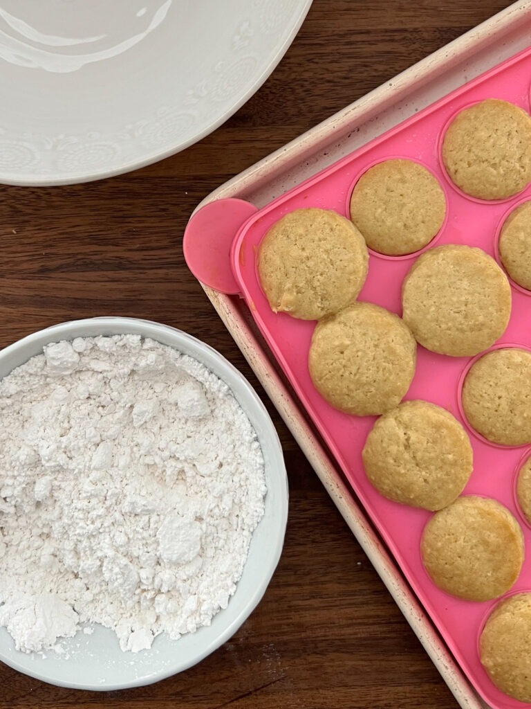 Baked donut holes near a bowl of powdered sugar.