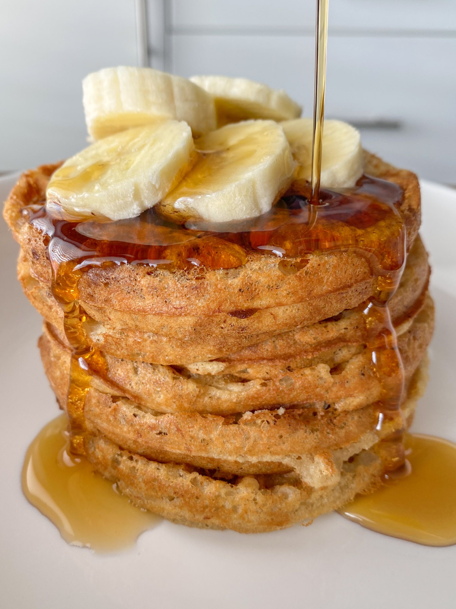 A stack of oat flour waffles topped with sliced banana and maple syrup.