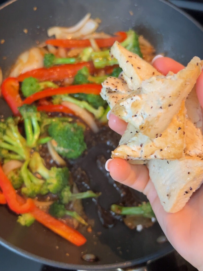 Adding tofu to a pan with vegetables.