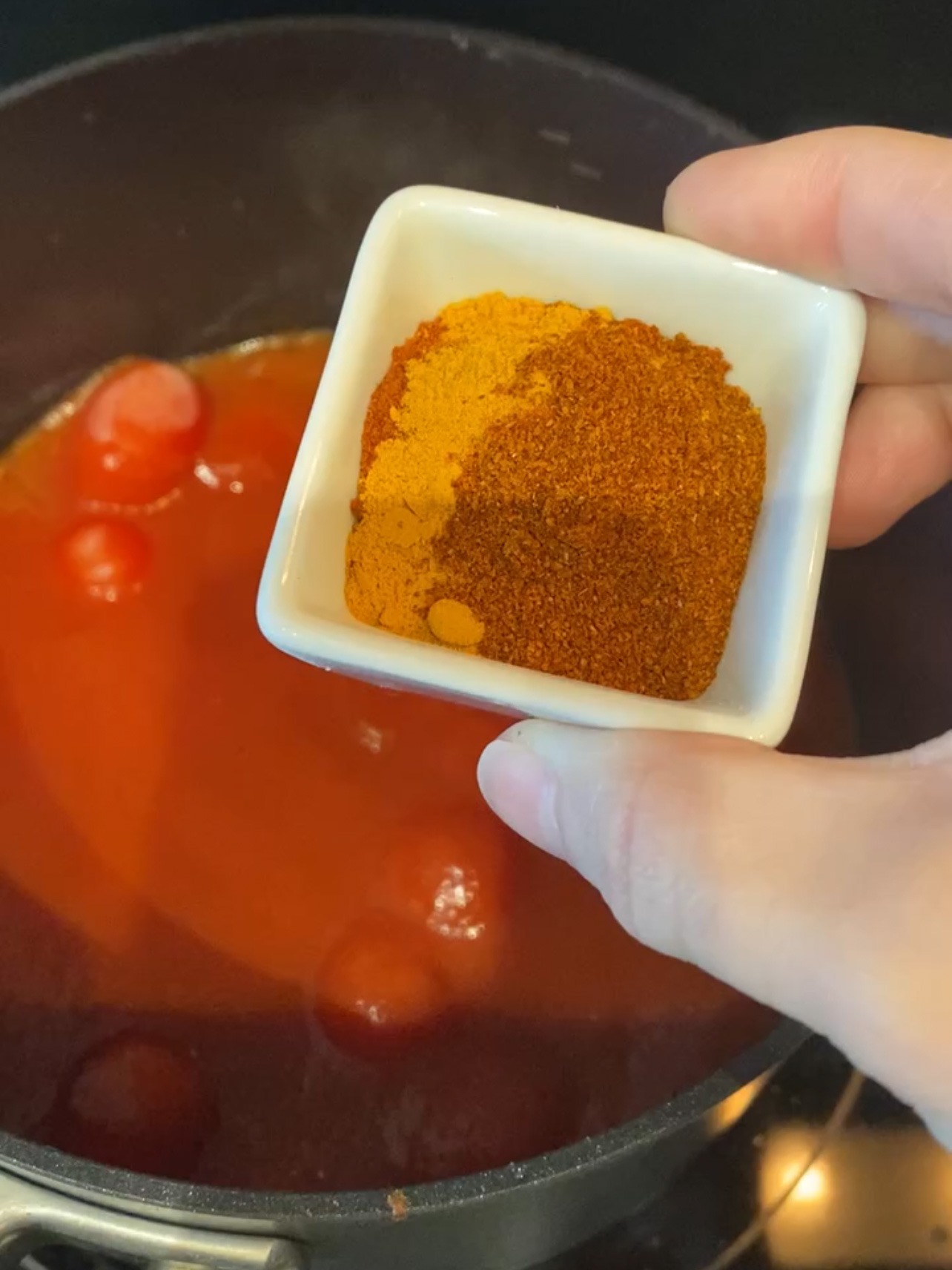 Adding spices to tomato sauce in a pan.
