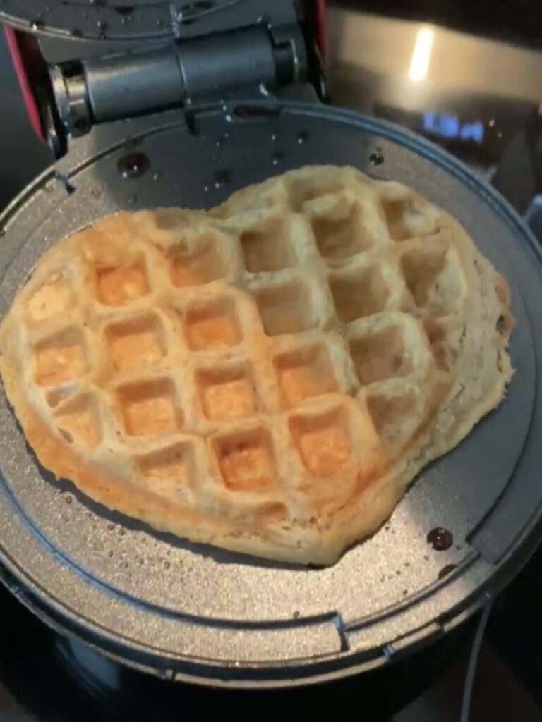 Heart-shaped waffle cooking in a waffle iron.
