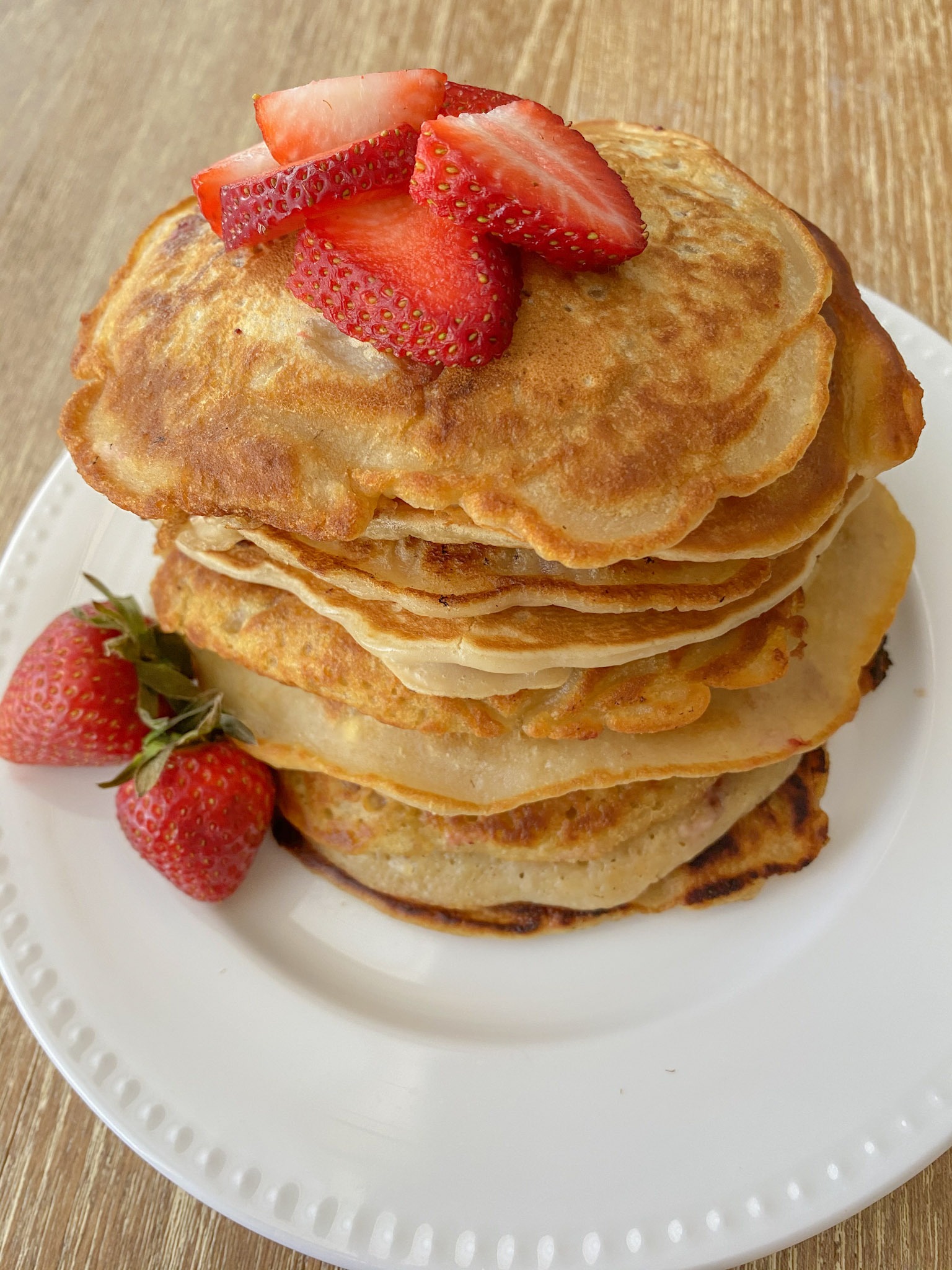 Strawberry pancakes served on a white plate with fresh strawberries.