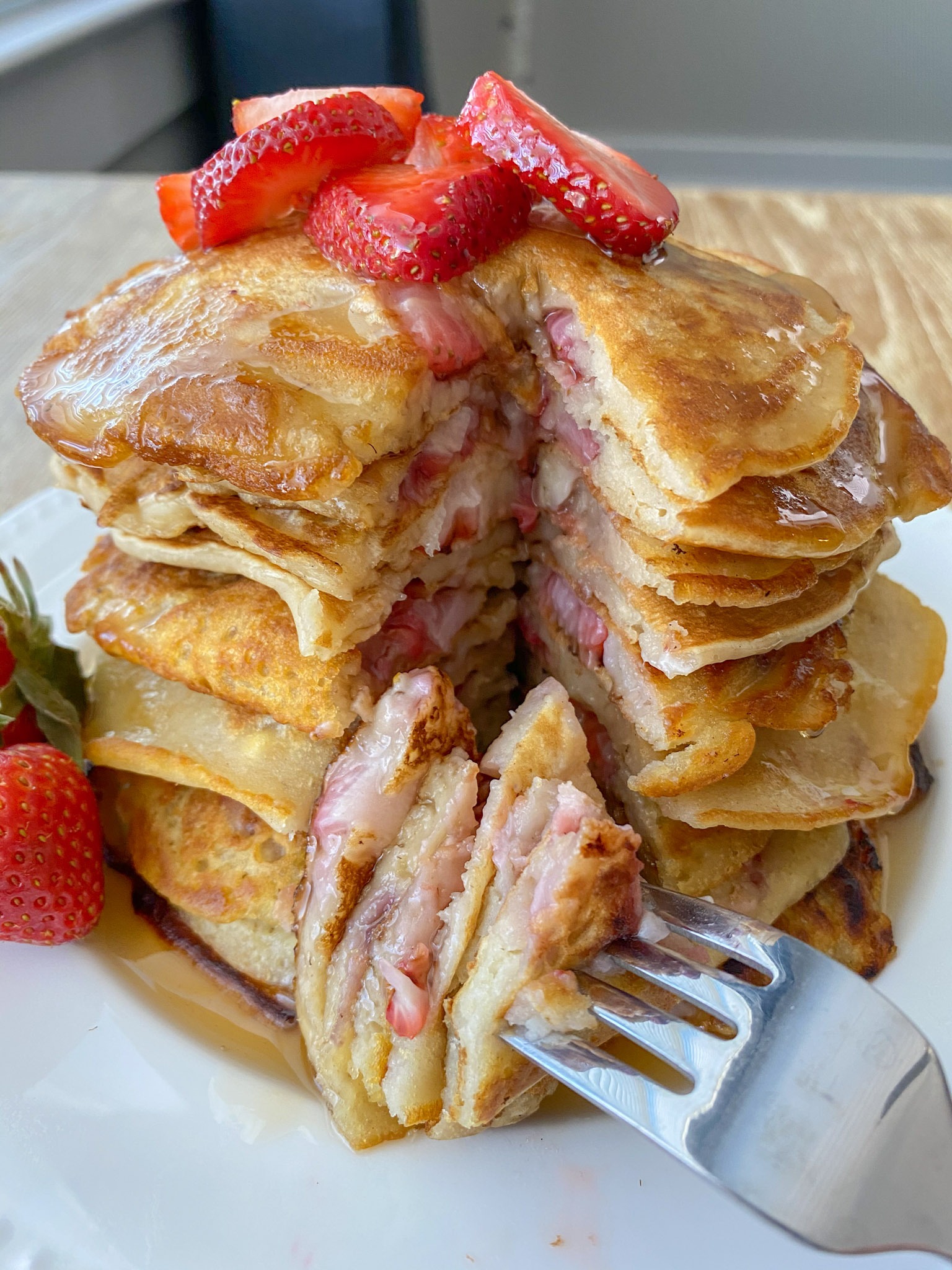 A large stack of strawberry pancakes with some on a fork.
