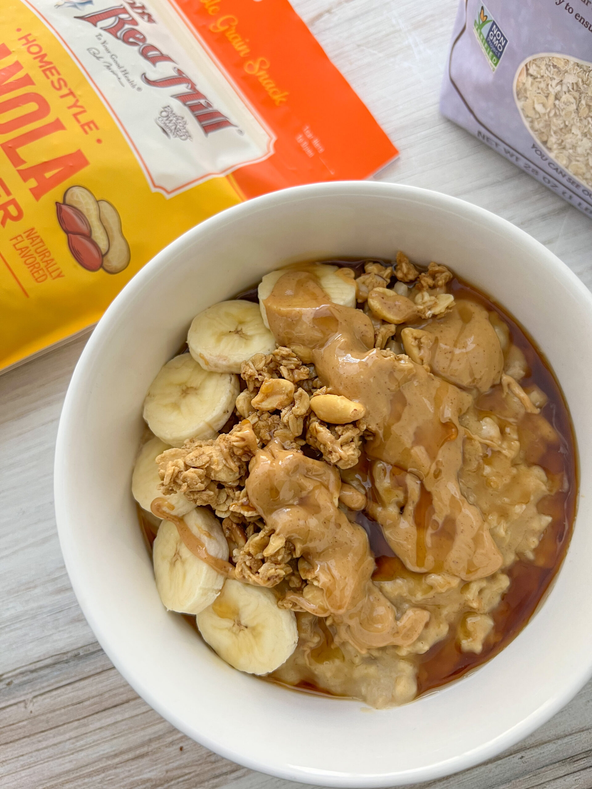 Peanut butter oatmeal in a white bowl with package of granola and oats in the background. 