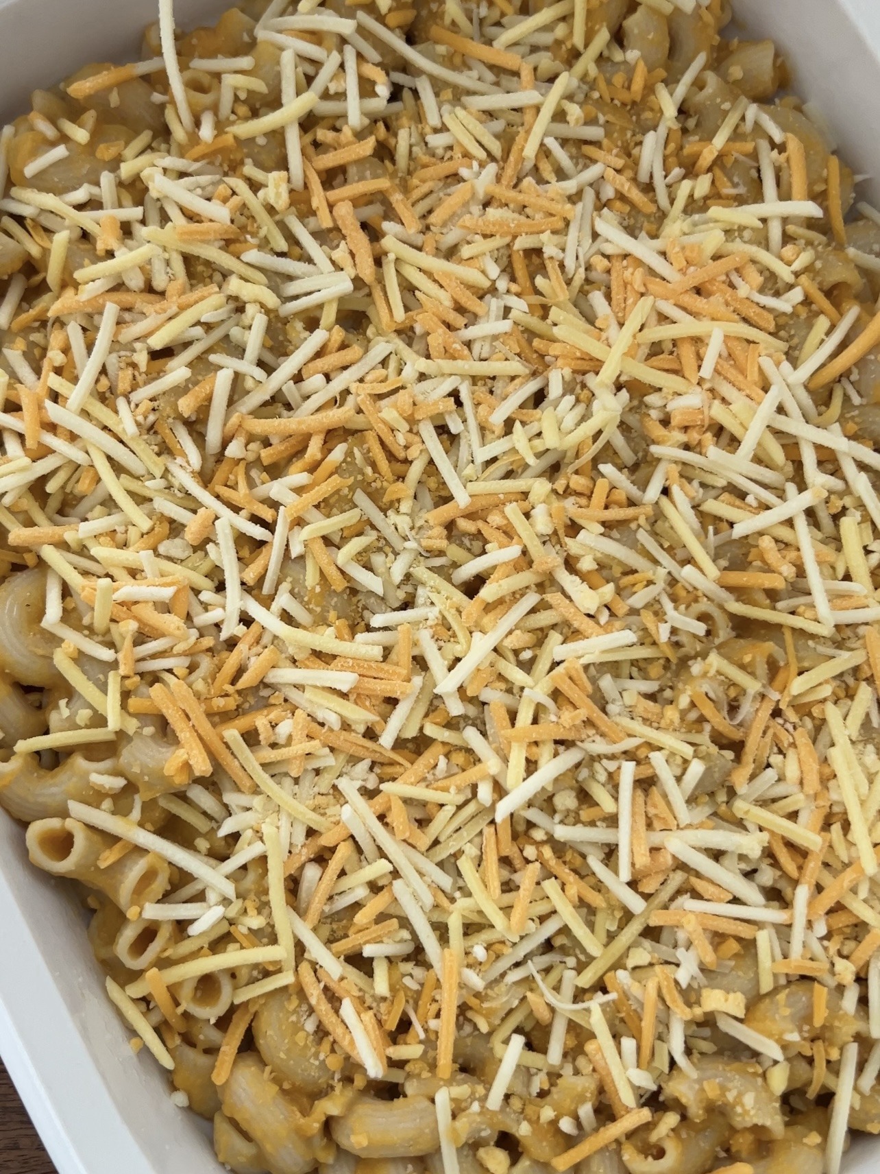 Step 6: Mix the sauce with the noodles and then transfer them all into a greased baking dish. Top with shredded vegan cheese and spray with olive oil.