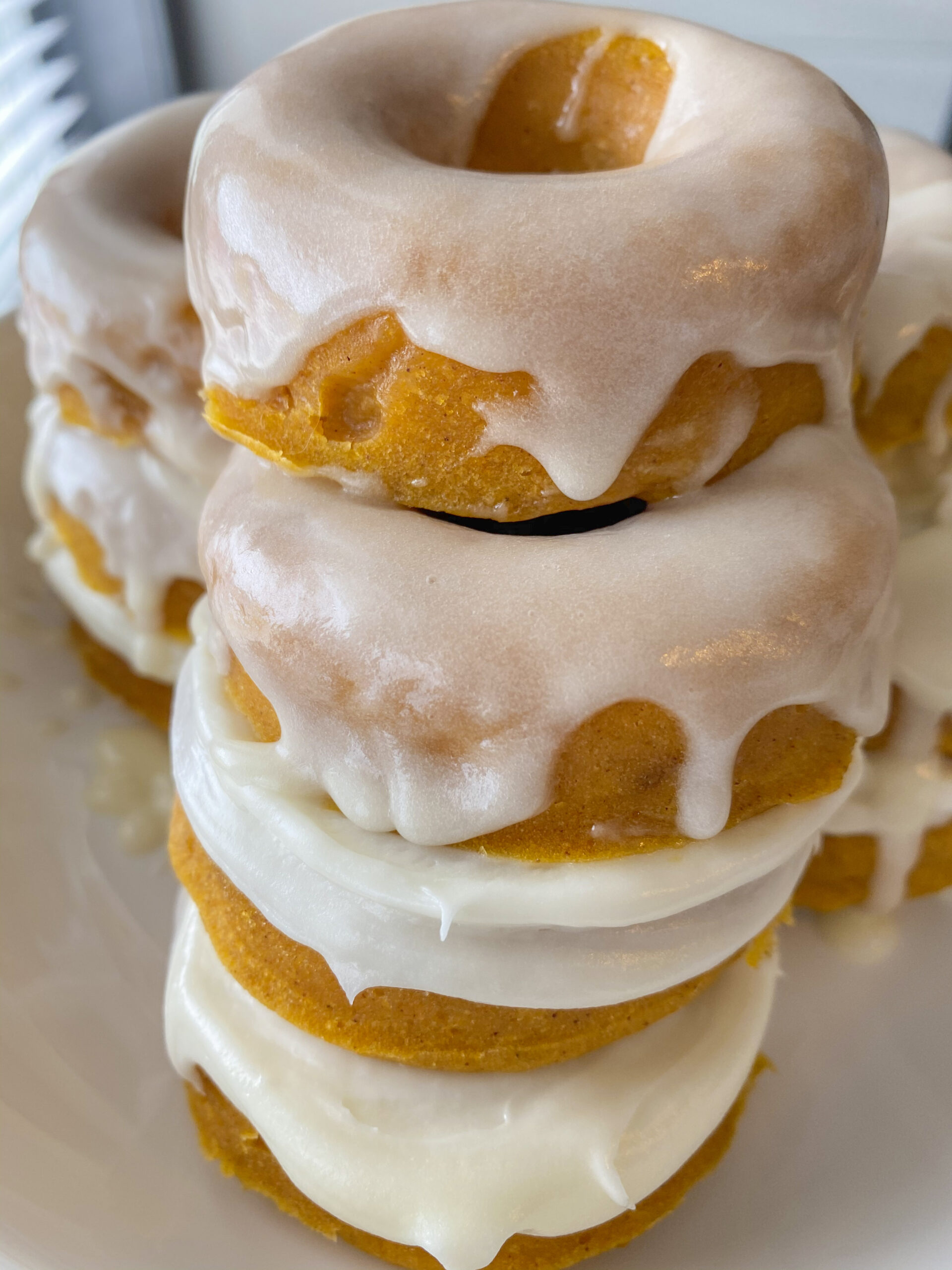 Pumpkin donuts stacked on top of each other with a cream cheese glaze on top.