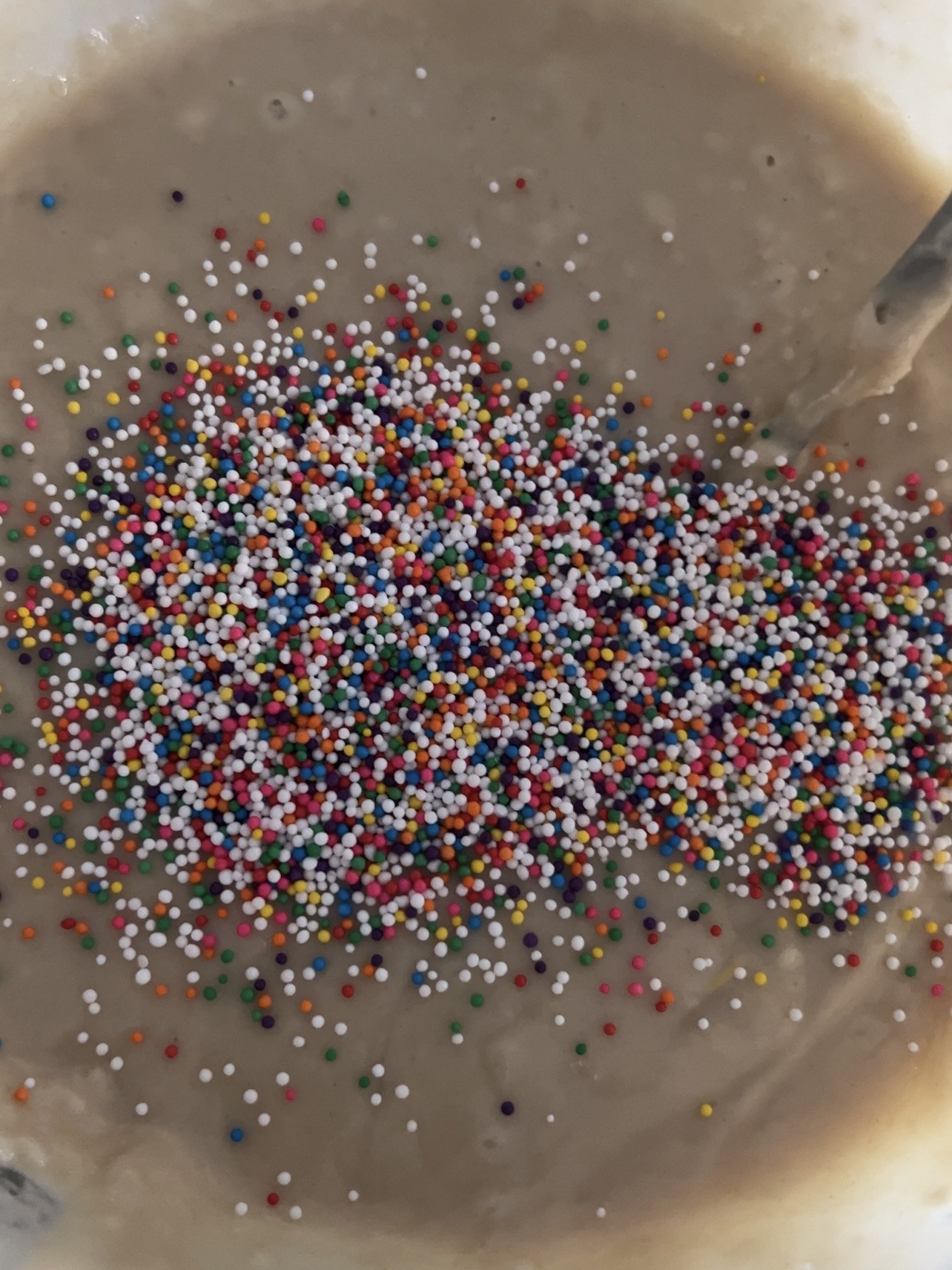 Adding rainbow sprinkles to cake batter in a large bowl.