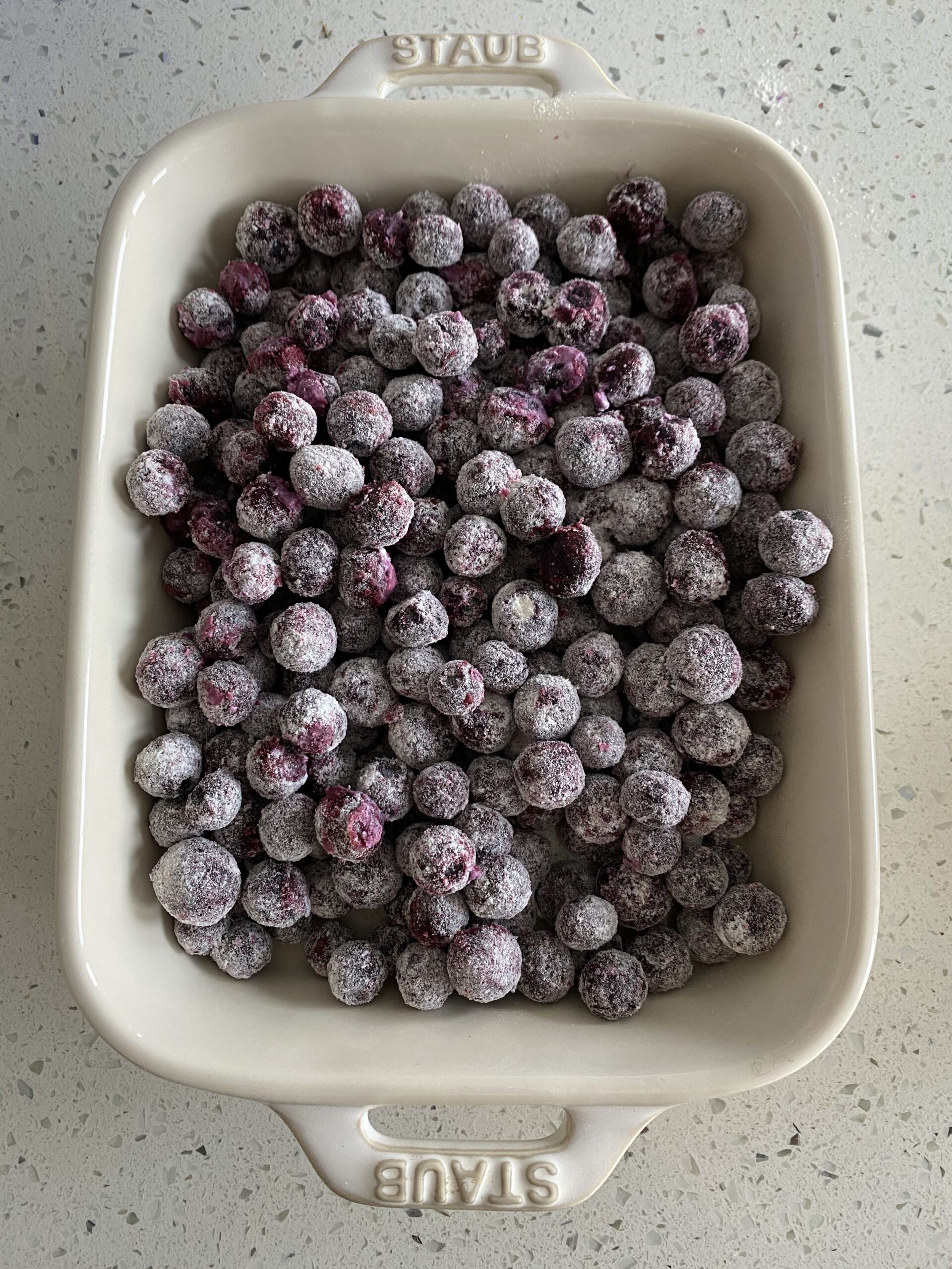 Frozen blueberries coated in flour in a white baking dish. 