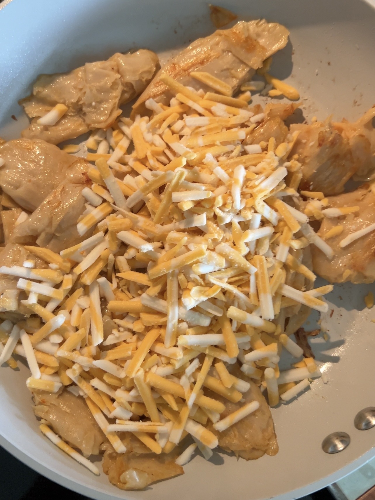 cooking the cheesy chicken by putting the cheese on top of the chicken in the skillet