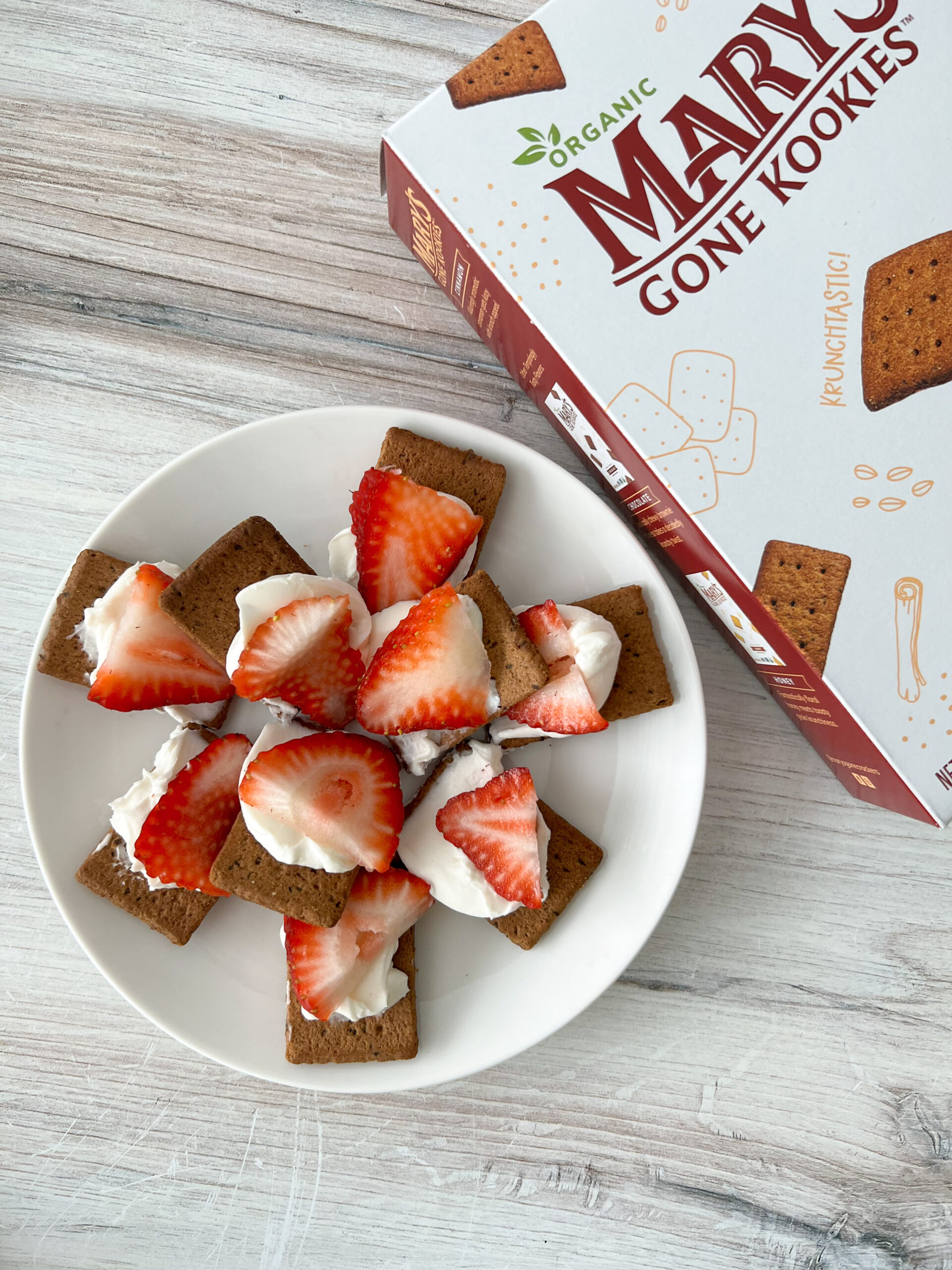 Crackers with cream cheese and strawberries on top on a white plate. 