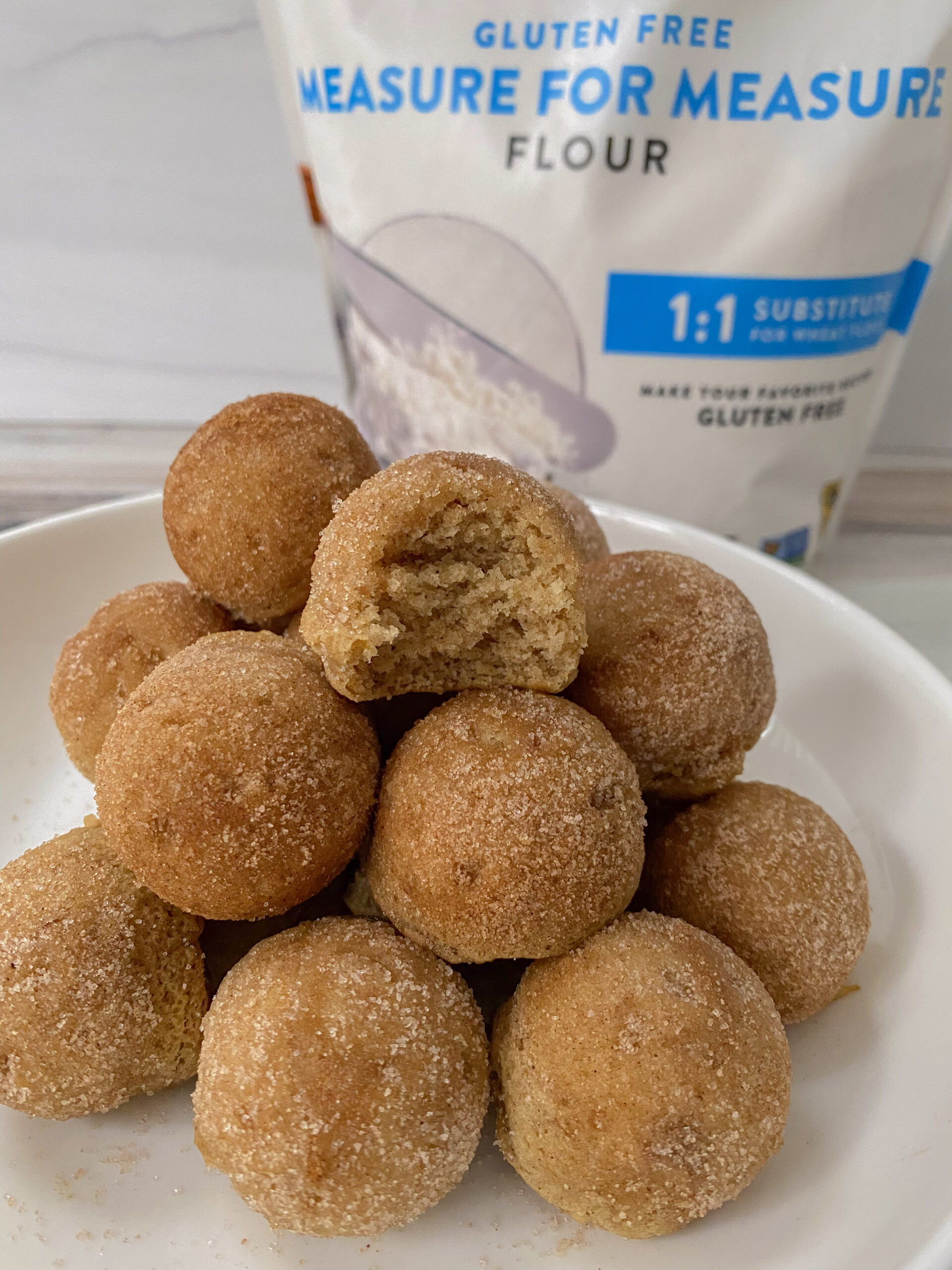 Donut holes with cinnamon sugar stacked on top of each other with a package of flour in the background. 