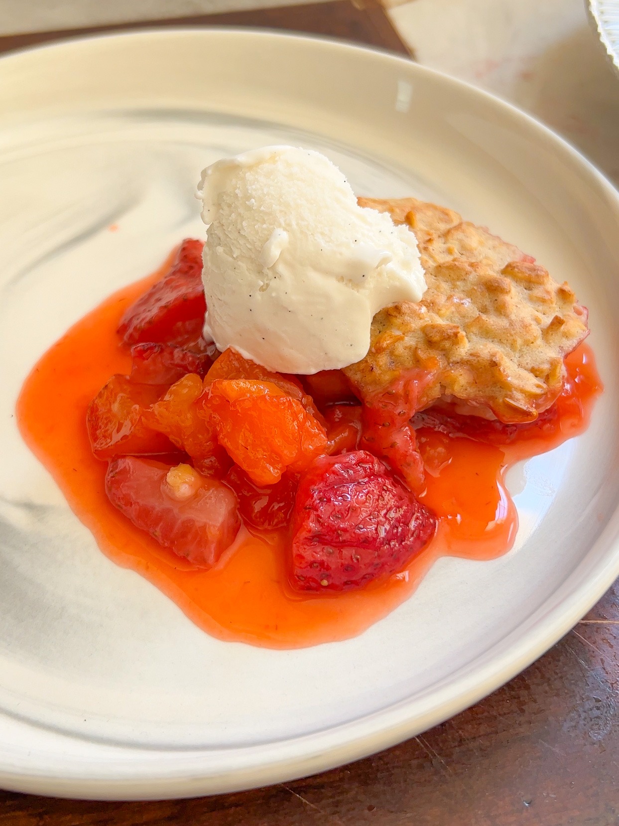 a plate with a scoop of strawberry peach cobbler topped with a scoop of ice cream